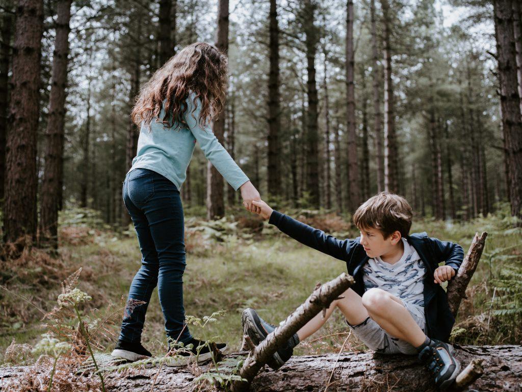 Foto meisje die jongen de helpende hand biedt in het bos_foto Annie Spratt via Unsplash